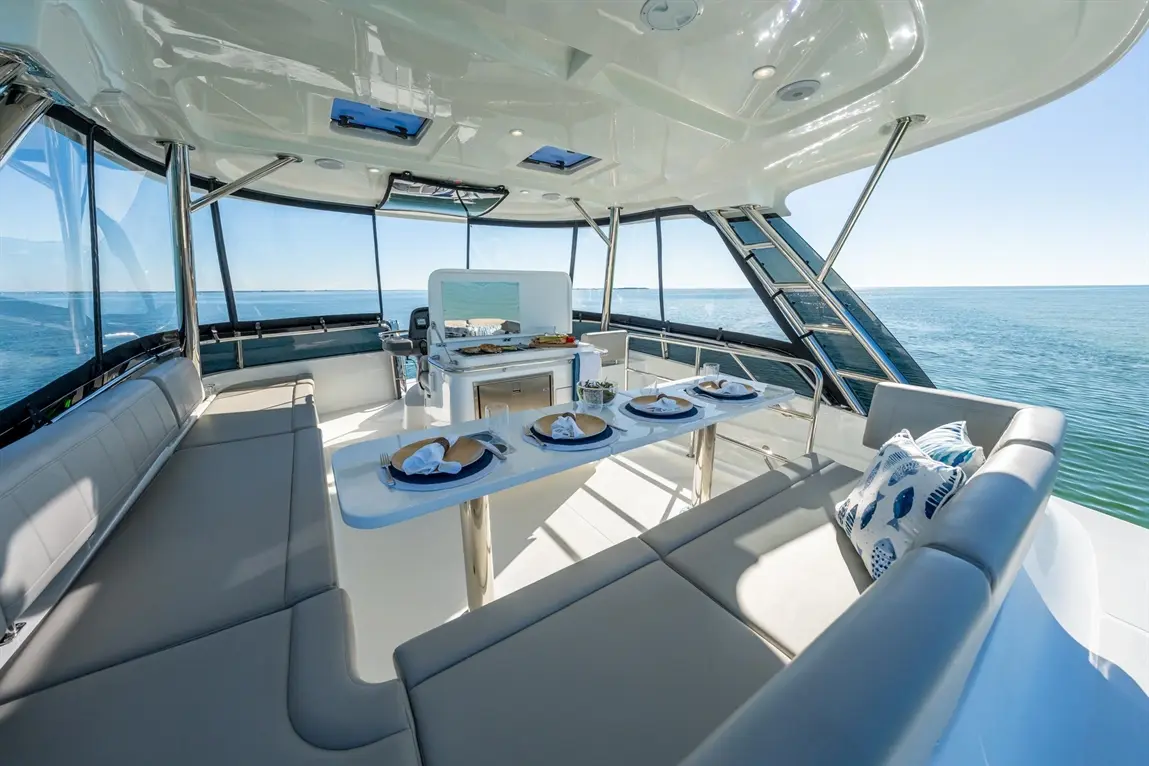 Luxurious yacht interior featuring a dining area with blue plates, cutlery, and cushions, overlooking calm waters.